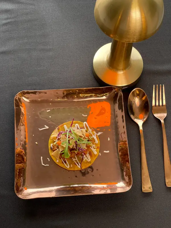 Delicate bites arranged on a square copper plate. Tajnuma, Agra.